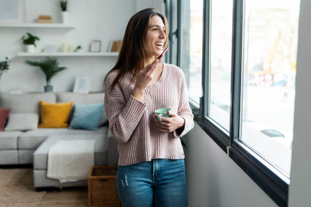 istock Pretty young woman using her mobile phone while drinking coffee near to the window in the living room at home 1399433064