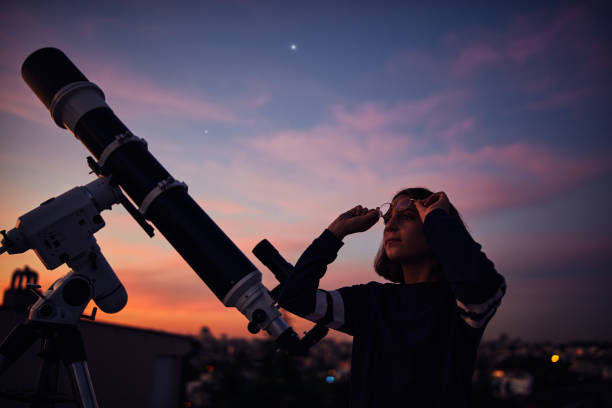 istock Girl with astronomical telescope stargazing under twilight sky. 1399433673