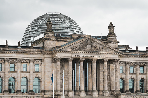 Bundestag building captured in an atmospheric mood and the German and European flag swinging in the wind.