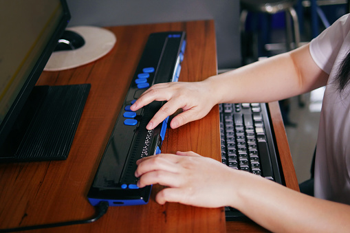 Las manos de las personas con discapacidad con ceguera utilizan una computadora con pantalla braille o terminal braille, un dispositivo de asistencia tecnológica para personas con discapacidad visual. photo