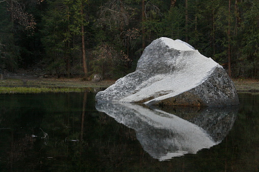 Large boulder rests in a lake in Yosemite with still water around it, creating a perfect reflection.
