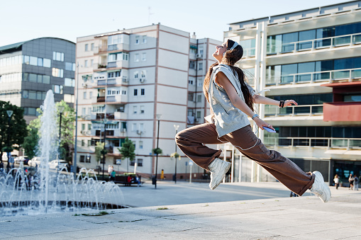 Beautiful girl dancing in a street. young woman with long hair jumping while listening to music.