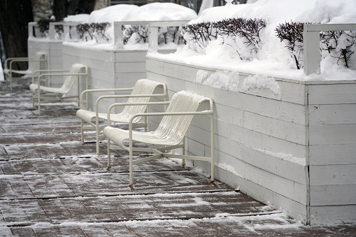 Metal benches on the snow-covered terrace with wooden decking.