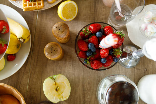Directly above shot of arrangement of fresh strawberries and blueberries in a glass bowl, salt and pepper shaker, lemon and apple half served on a dining table, to be enjoyed during a meal.