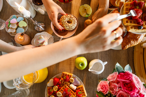 Directly above shot of hands of unrecognizable females reaching for various sweet foods served on a dining table, during breakfast, brunch of afternoon tea.