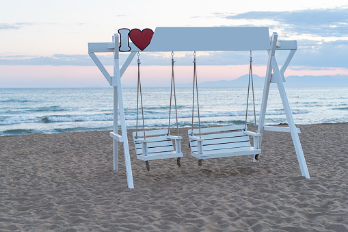 Romantic white wooden swing set on the beach by sunset.