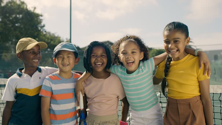 A group of children playing tennis. Portrait of happy, cute, diverse tennis players standing together and smiling on the court