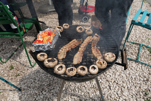 Grilling mushroom, bacon and vegetables on a barbecue grill spheric fire pit at a garden party