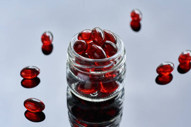 Krill oil pills or softgels in a glass jar on a glossy background stock photo