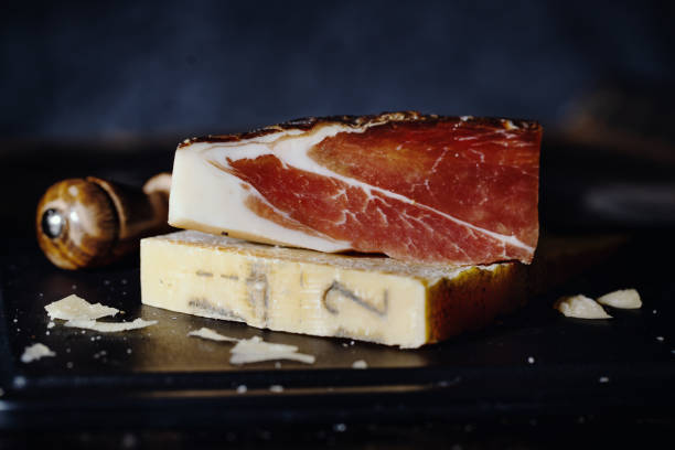 Parmesan cheese and meat on wooden board Expensive parmesan cheese with prosciutto meat and knife on wooden board. Italian food concept grana padano stock pictures, royalty-free photos & images