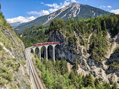 Landwasser viaduct in the Davos mountains near Filisur. Beautiful old stone bridge with a moving train. Spring Time