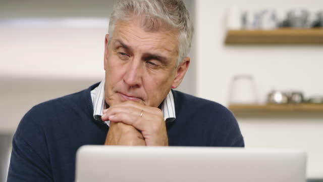 A senior man planning his finance, paying bills and looking unhappy while using laptop at home. A mature man working online with a computer and feeling confused, stressed and unsure