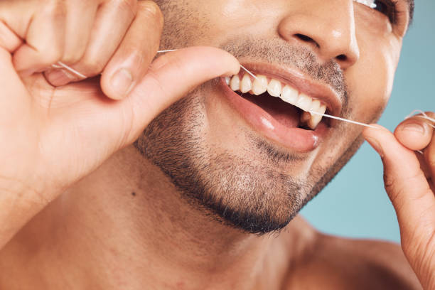 istock Closeup of one mixed race man flossing his teeth against a blue studio background. Guy grooming and cleaning his mouth for better oral and dental hygiene. Floss daily to prevent tooth decay and gum disease 1399453192