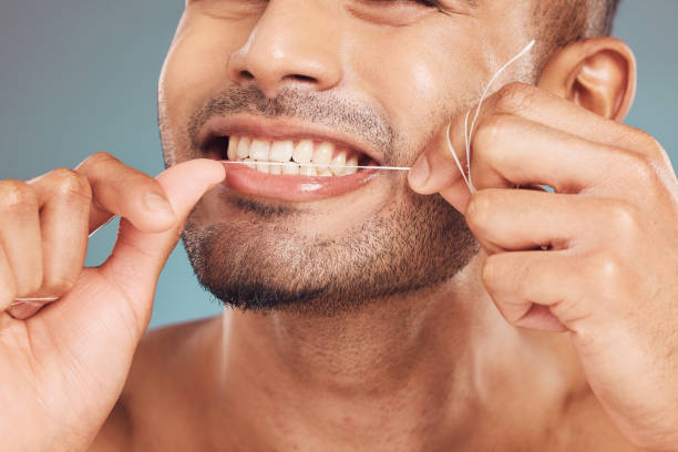 istock Closeup of one mixed race man flossing his teeth against a blue studio background. Guy grooming and cleaning his mouth for better oral and dental hygiene. Floss daily to prevent tooth decay and gum disease 1399453264