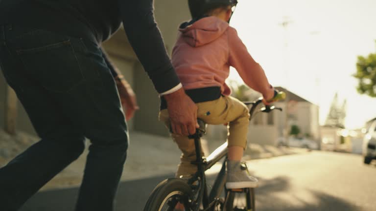 Little boy riding a bicycle with his grandfather. A mature man and his grandson learning to ride a bike outdoors. Cute little boy and a senior relative having fun family time in the street