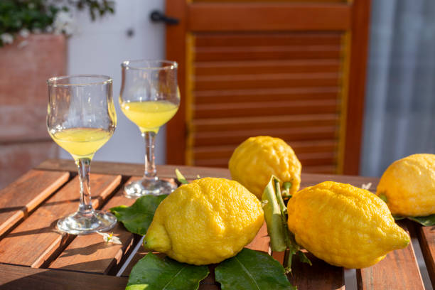 limones con hojas, limonada o limoncello en vaso de cristal, sobre una mesa de madera en la terraza. - liqueur glass fotografías e imágenes de stock