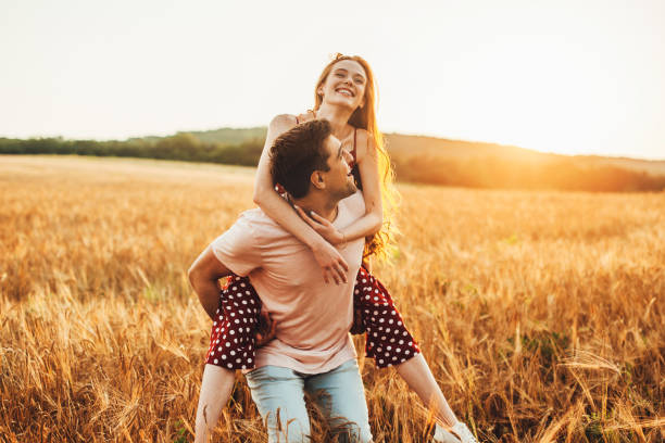 istock Front view of a boy having fun with his girlfriend walking while dragging her onback through the sprouted wheat field. Smiling man. 1399471311