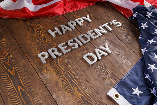 words happy presitdents day laid with silver metal letters on wooden surface near crumpled US flag