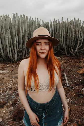Red-haired girl with hat looking at camera in an environment with cacti