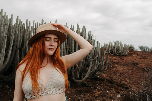 Relaxed redhead girl putting on her hat with the desert and cacti in the background