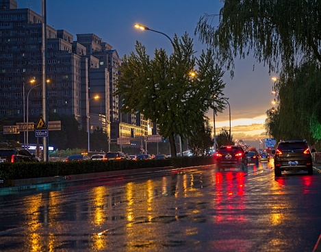 Road in city center of Beijing after heavy rain, Last rays of sun start come out behind of clouds and makes road reflected different kind of colours.