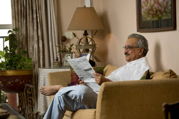 istock Old man reading newspaper on sofa at home 1399496497