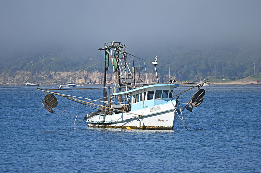 Old fishing trawler on the water with fog above it.
