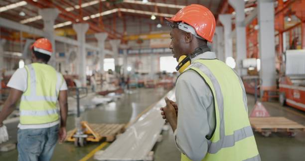 istock Rear view. Two professional industrial engineer or worker or foreman in metal work, wear personal protective equipment, walking to working in metal part production line at manufacturing factory. 1399497448