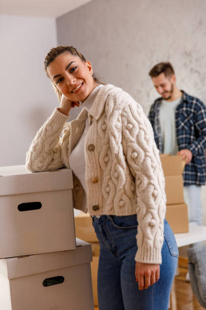 istock Young woman leaning against a stack of cardboard boxes and smiling at camera 1399499823