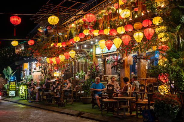 人々はホイアンの町の川の近くにあるカラフルなレストランで休んでいます。ベトナム - hoi an ストックフォトと画像