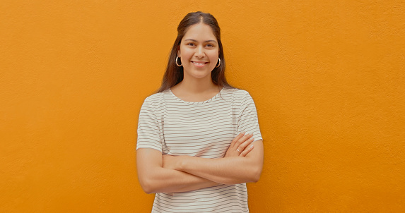 Portrait of a confident young woman, isolated on a yellow background. A smiling mixed race female standing with her arms crossed, looking at the camera