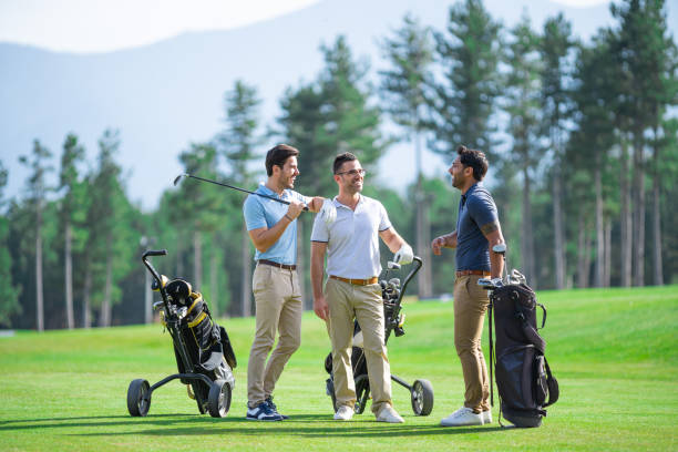 Group of male golfer friends, playing golf on a beautiful sunny day, talking and smiling while standing on golf course stock photo