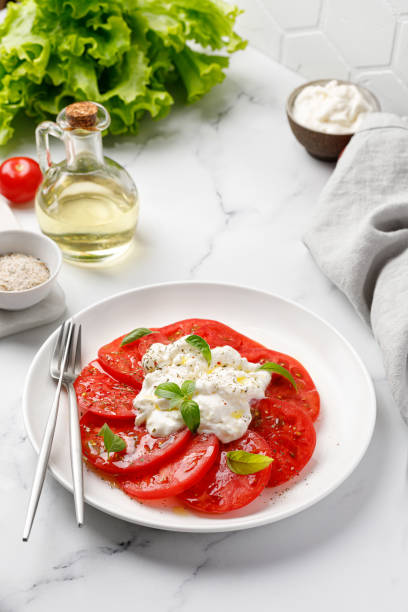 istock Salad with Stracciatella cheese on white plate with fork, oil, fresh basil and tomatoes. Italian Stretched curd cheese product in Stracciatella salad. Close up 1399510866