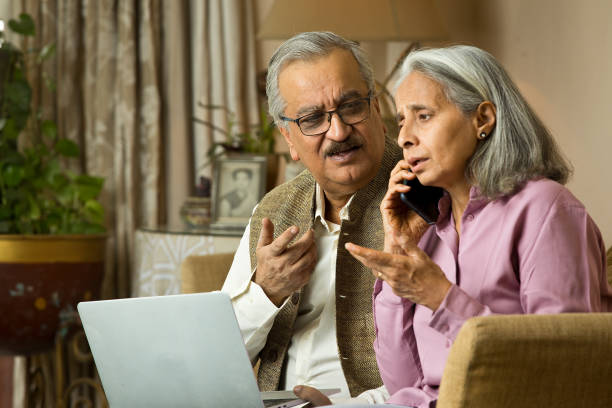 vieux couple stressé utilisant un ordinateur portable et parlant sur un téléphone portable à la maison - women computer couple surprise photos et images de collection