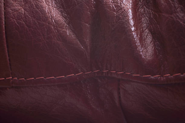 Two pieces of antique leather with a reddish tint are sewn in the middle with a strong rope in a cross-shaped seam horizontally, close-up.