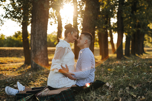 Young couple in love sitting and hugging in beautiful nature at sunset, side view
