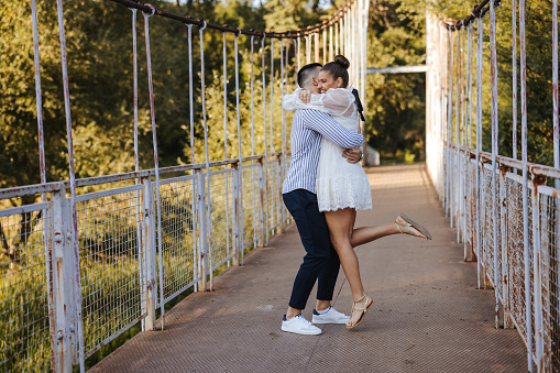 Young romantic couple standing and hugging on footbridge in nature on sunny day