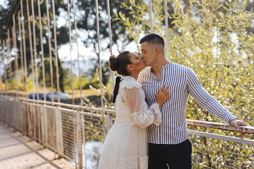 Young romantic couple standing and kissing on footbridge in nature on sunny day