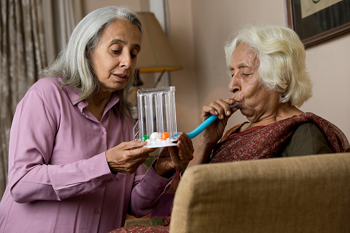 Elderly woman supporting her female friend after using a spirometer to stimulate lung