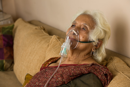 Senior woman with oxygen mask at home