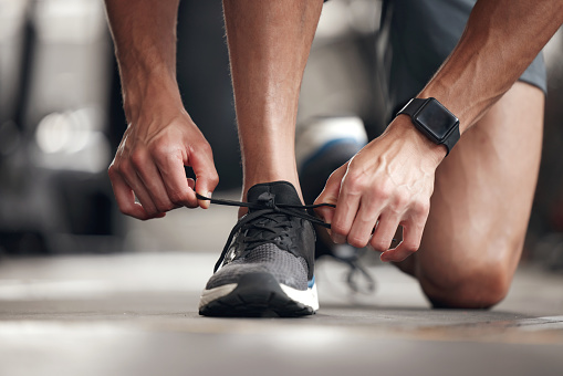 Closeup of one mixed race man tying his shoelaces while exercising in a gym. Guy fastening sneaker footwear for a comfortable fit and to prevent tripping during a training workout in a fitness centre