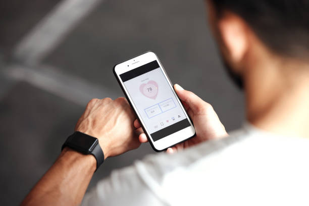 Closeup of one mixed race man checking health applications on digital wristwatch and cellphone for exercise in a gym. Guy from above wearing fitness tracker on arm and reading data about heart rate, body temperature and blood pressure on a phone screen primer plano de un hombre de raza mixta revisando aplicaciones de salud en un reloj de pulsera digital y un teléfono celular para hacer ejercicio en un gimnasio. chico de arriba usando un rastreador de ejercicios en el brazo y leyendo datos sobre la frecu