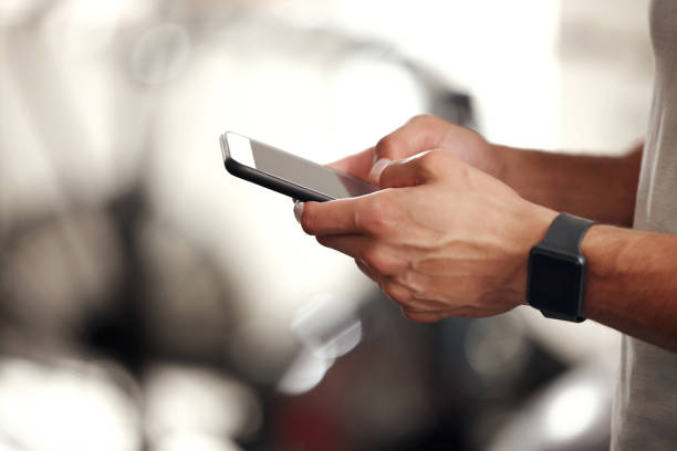 istock Closeup of one fit mixed race man using a cellphone while taking a break from exercise in a gym. Hands of a guy texting and browsing fitness apps online while checking social media during a rest from training workout 1399520069