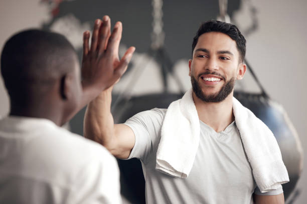 un giovane ispanico fiducioso che dà il cinque al suo amico mentre si esercita in palestra. felice ragazzo di razza mista che rimane motivato mentre festeggia la fine di un allenamento di successo con un istruttore in un centro fitness - amicizia tra uomini foto e immagini stock