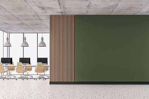 Empty office interior with a large empty khaki green colored plaster wall and partly hardwood paneled wall with copy space on terrazzo floor. Wordesks, lighting equipment, computer equipment and windows in background. 3D rendered image.