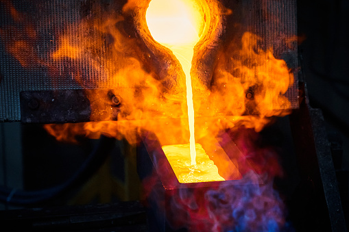 Filling graphite casting form with hot melted gold metal in shielding gases sphere in production plant extreme close view