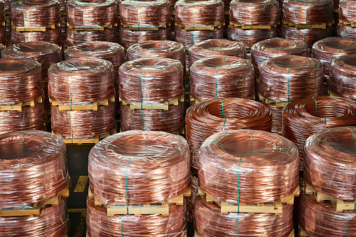 Rows of copper cable coils wrapped with plastic foil on wooden pallets in spacious storage of contemporary production plant