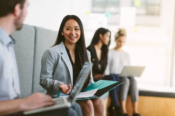 multiracial young woman sits to discuss with work colleagues plans and ideas in modern coworking shared business office - chinese ethnicity latin american and hispanic ethnicity multi ethnic group business person imagens e fotografias de stock