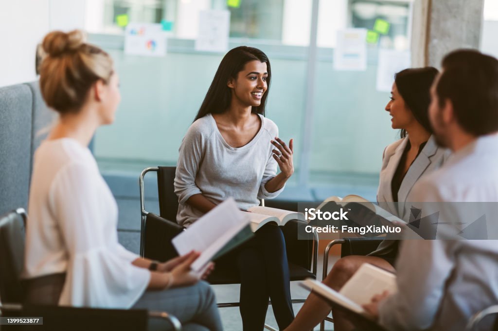 Young Indian ethnicity woman leading discussion while going over books in meeting in modern interior space Religion Stock Photo