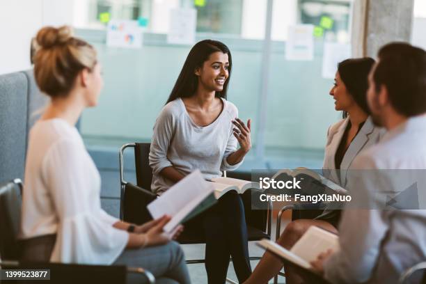 Young Indian Ethnicity Woman Leading Discussion While Going Over Books In Meeting In Modern Interior Space Stock Photo - Download Image Now